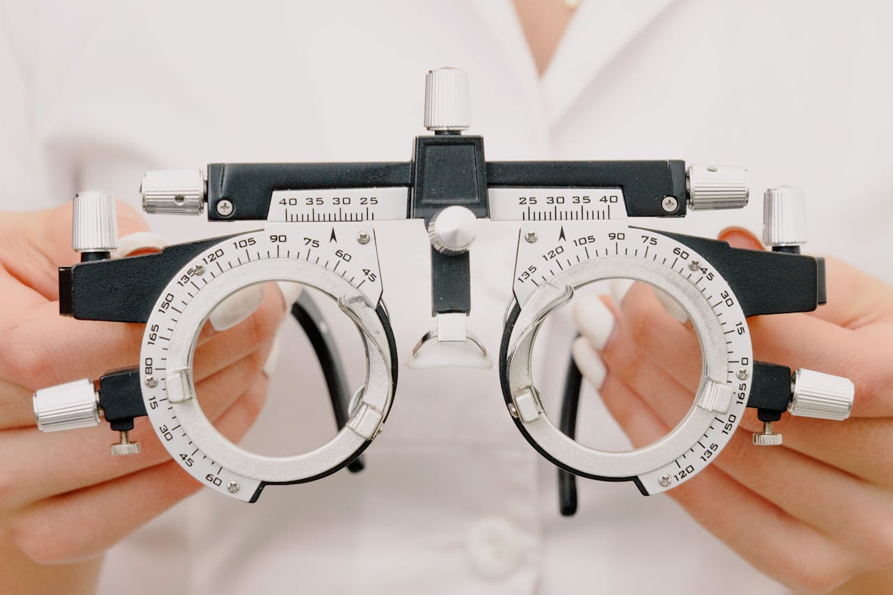 Crop anonymous female optometrist wearing medical robe holding modern trial frame with lenses in hands in modern optometry clinic